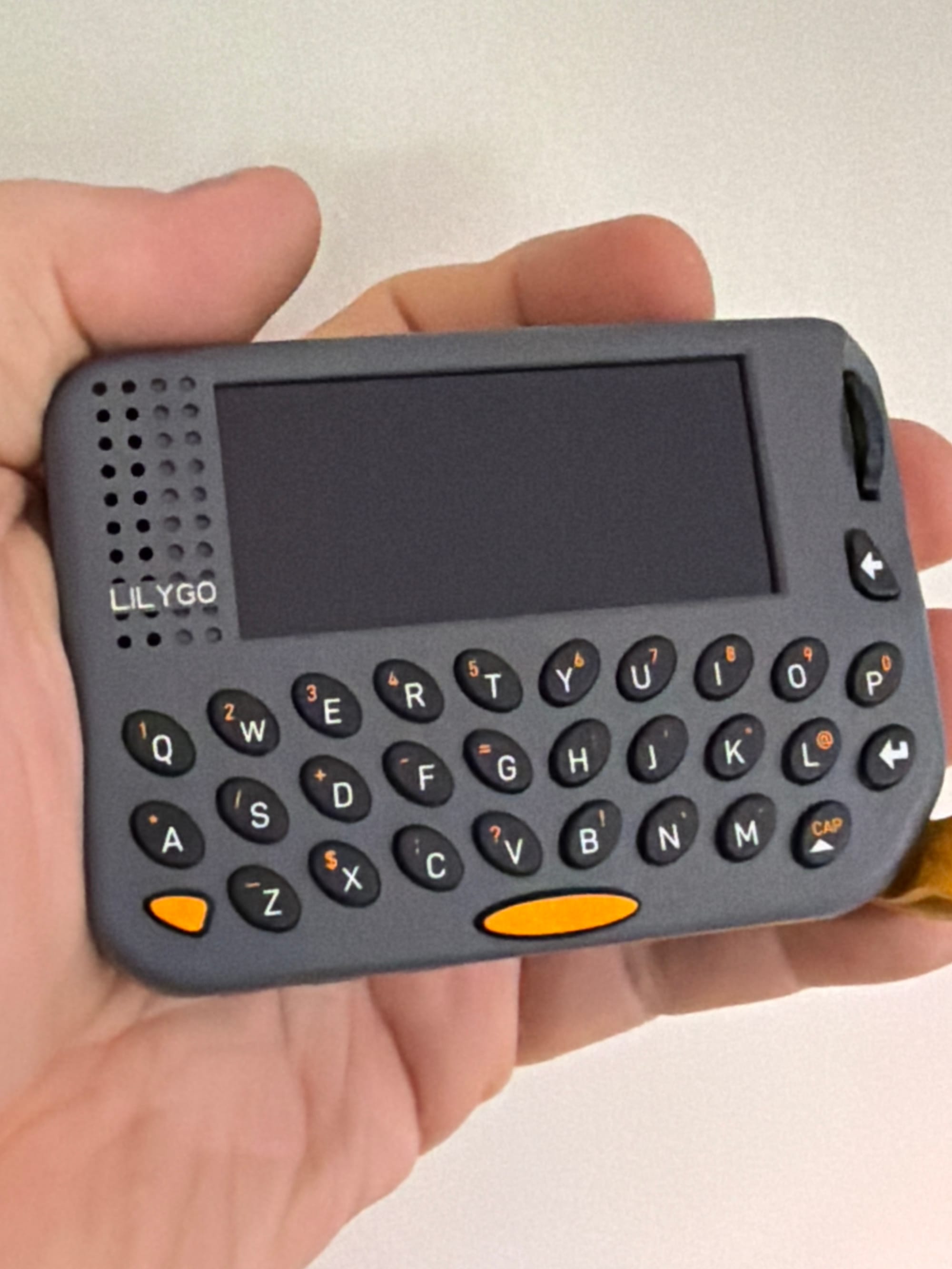 Closeup of a palm-sized standalone MeshCore companion device with a chicklet keyboard and small screen.