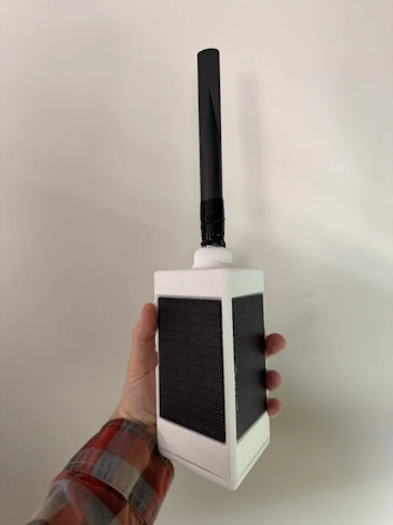 A triangular box with two small solar panels and an antenna, held in a person's hand for scale. The box and antenna are each about 7 inches long.